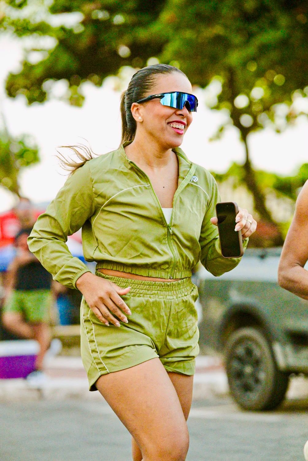 Jaine correndo sorridente de óculos esportivos e conjunto verde-oliva